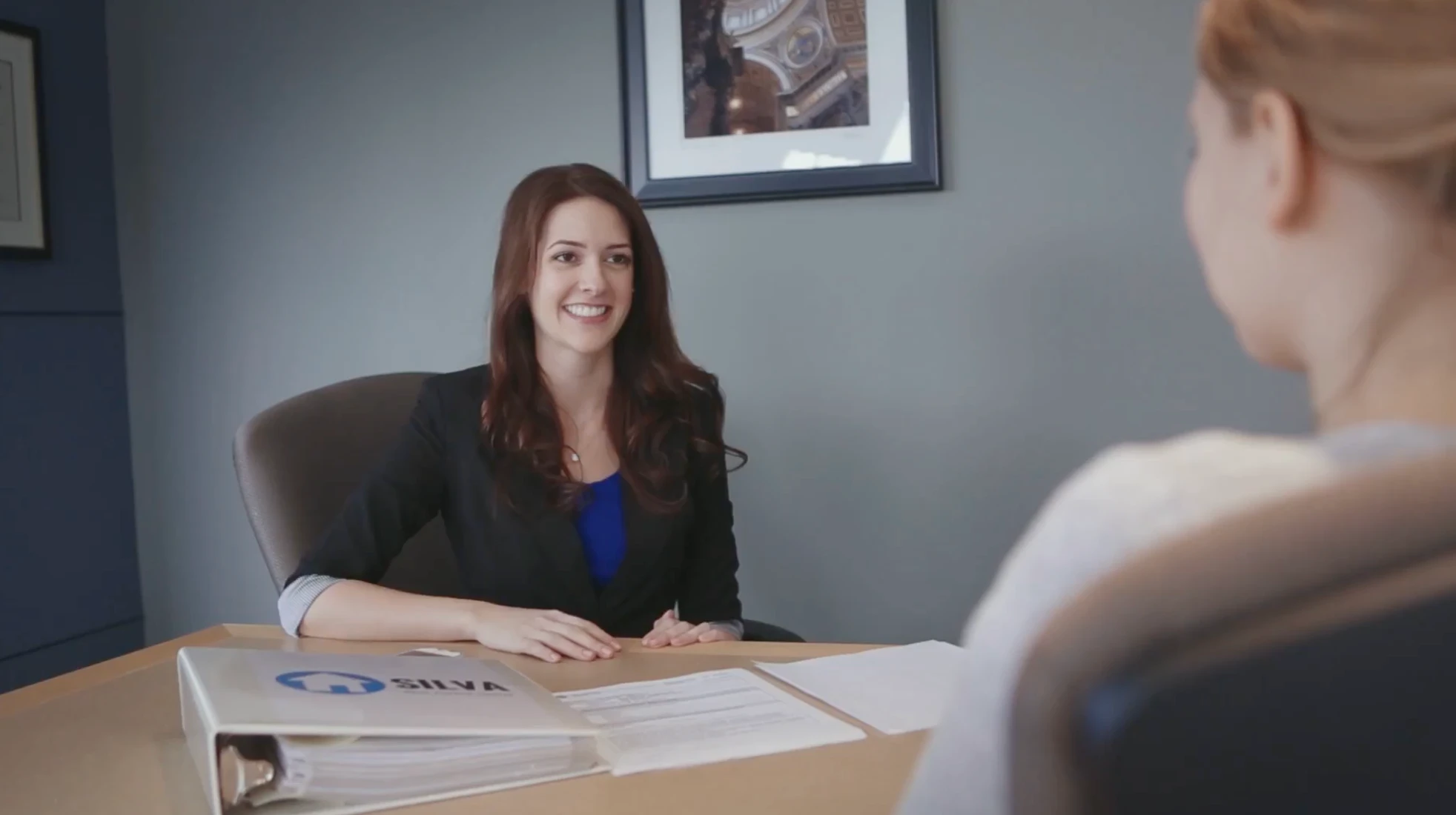 A client meeting from the commercial — two people across a desk, branded materials in view.